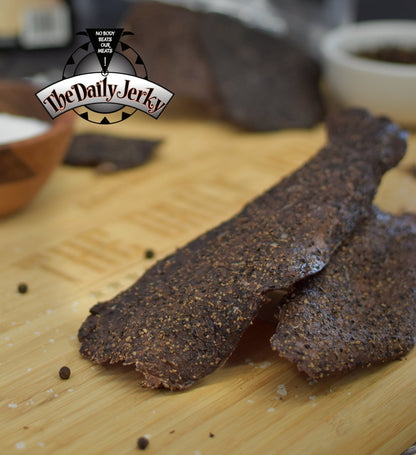 Salt and pepper beef jerky from The Daily Jerky served on a wooden board as a clean high protein snack